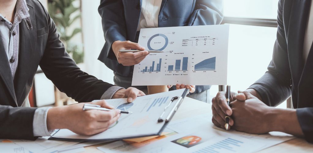 Three people holding financial graphs with pens in their hands, pointing to the graphs.